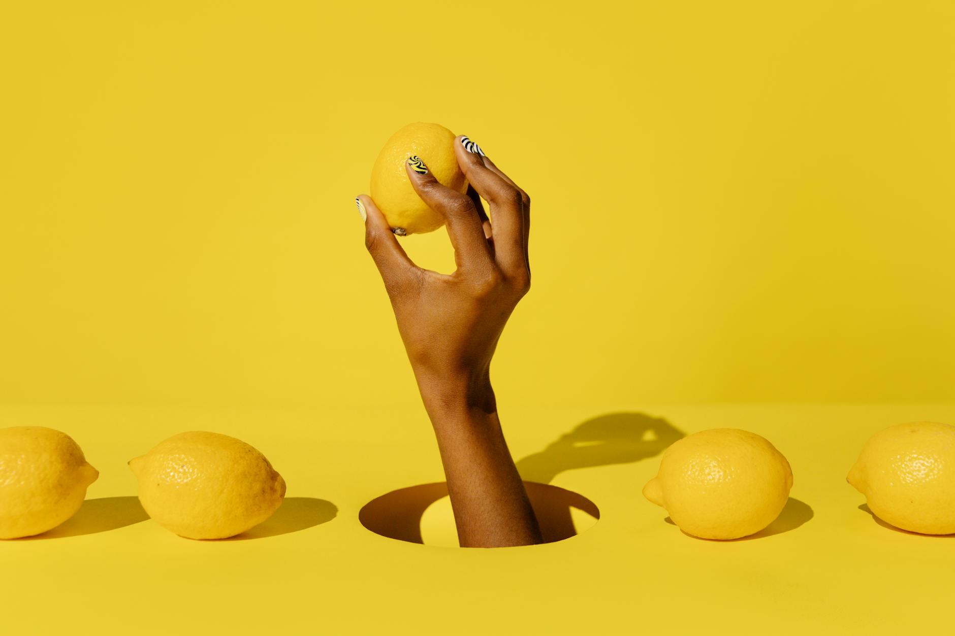 A hand holding a fresh lemon against a bright yellow background, symbolizing renewal and sensitivity restoration