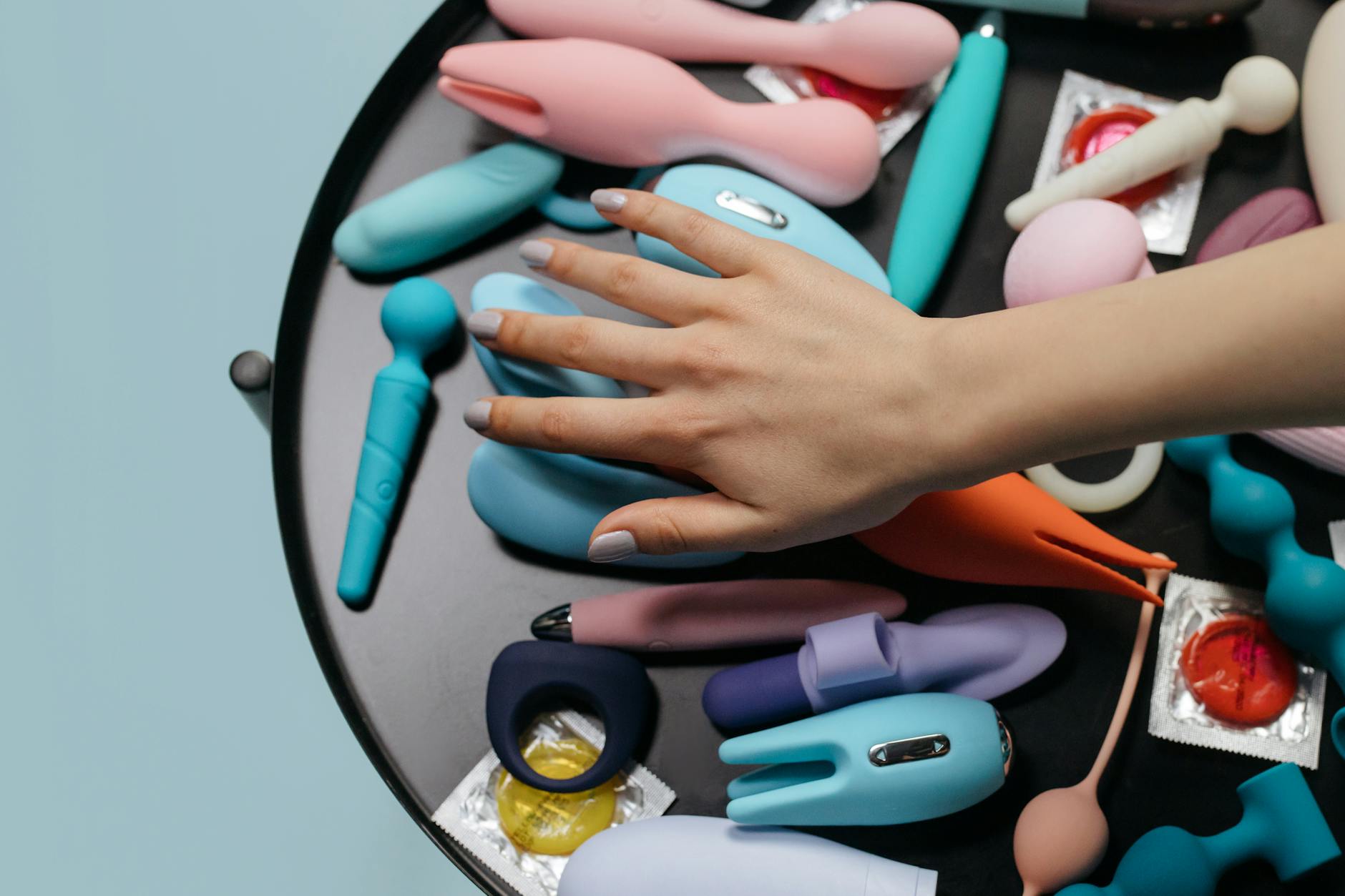Hand reaching toward colorful lemon vibrators and adult toys arranged on a table