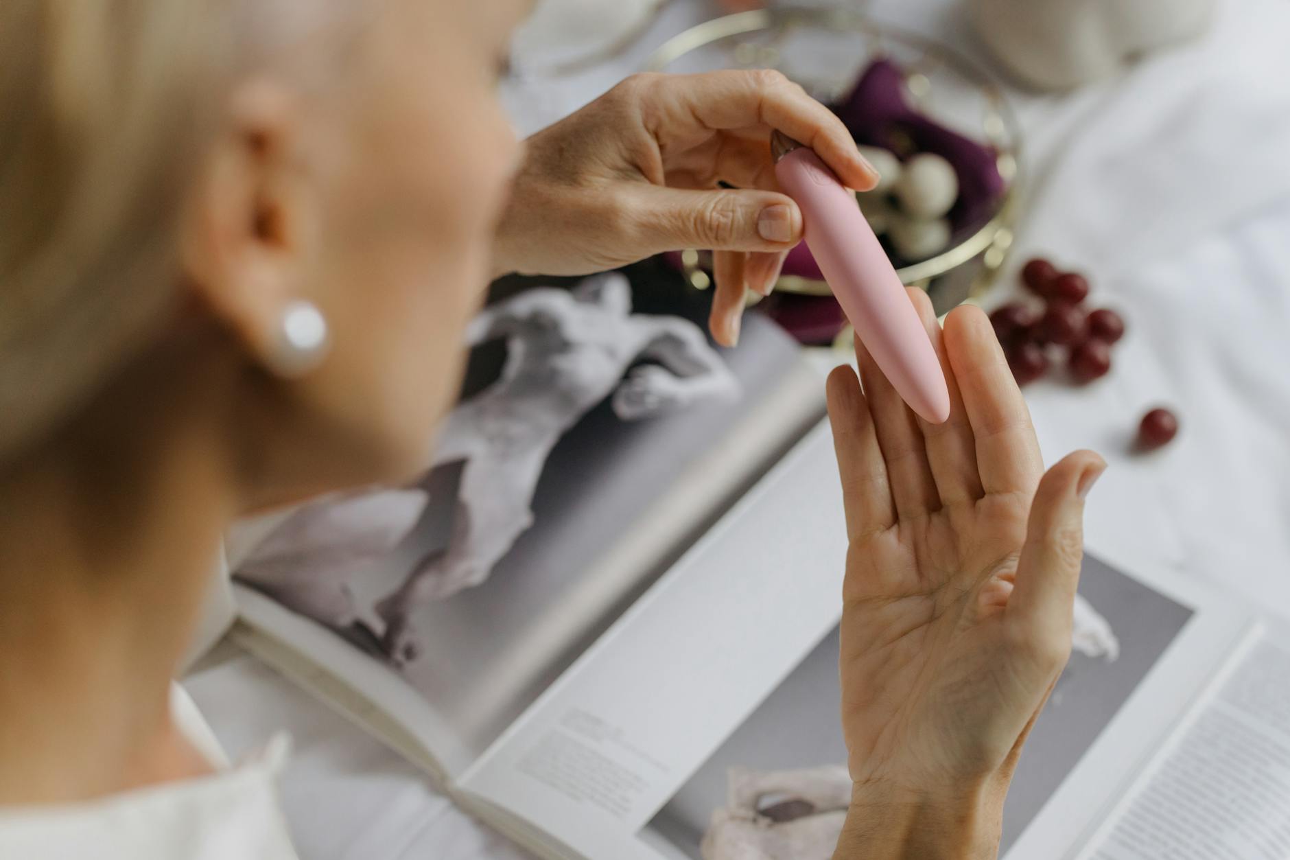 Close-up of a woman's hand holding a pink vibrator next to art books, representing reclaiming intimacy after postpartum recovery.