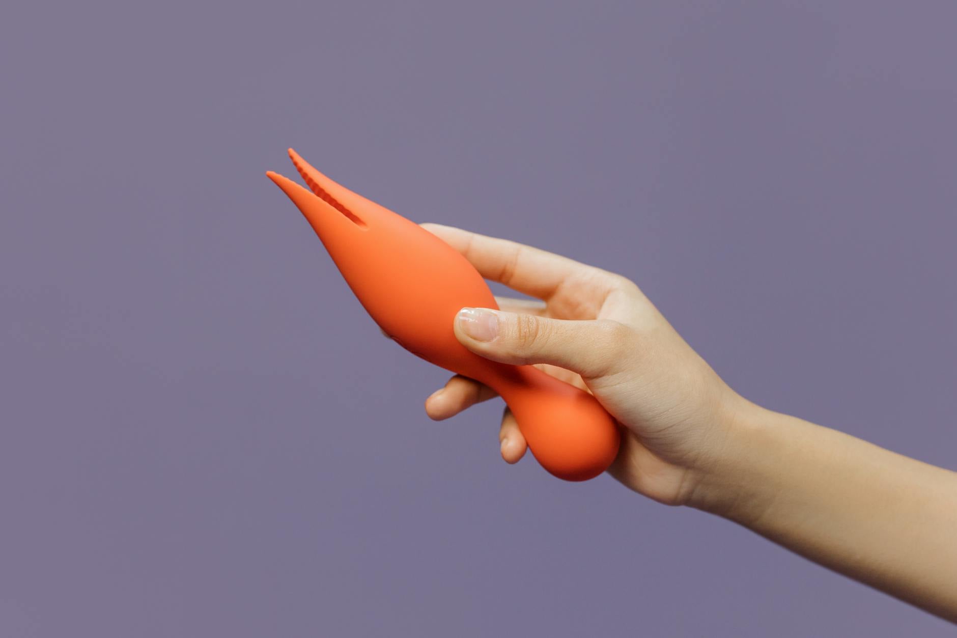 Hand holding a yellow lemon clitoral vibrator against a minimalist purple backdrop