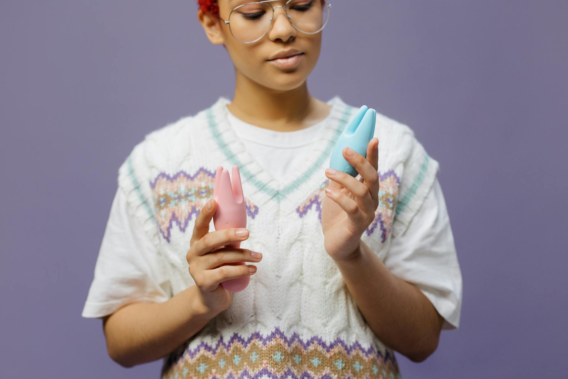 Woman holding blue and pink vibrators, exploring pleasure at her own pace and comfort level.