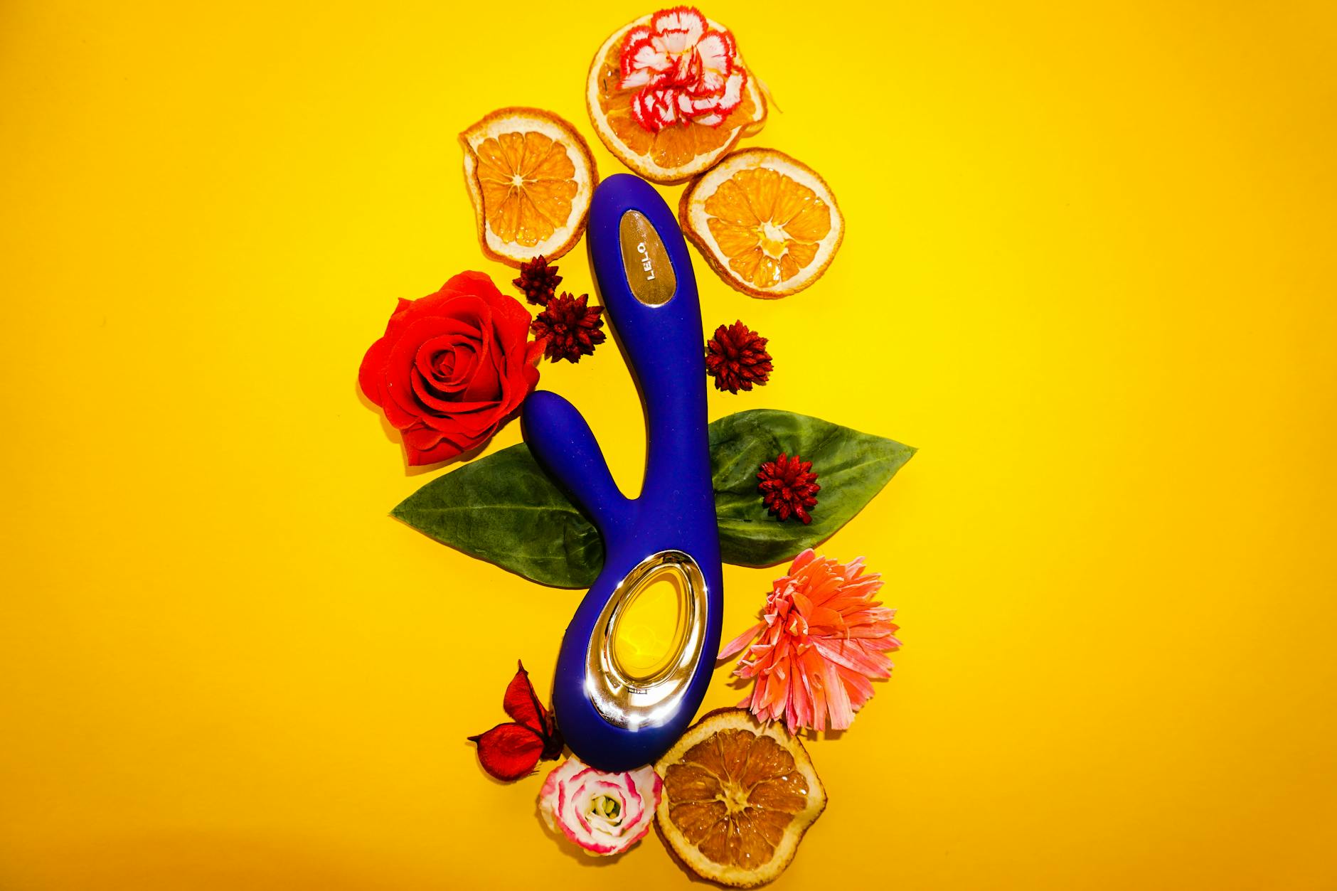 A bright lemon-yellow vibrator surrounded by fresh citrus and flowers on a warm yellow background.